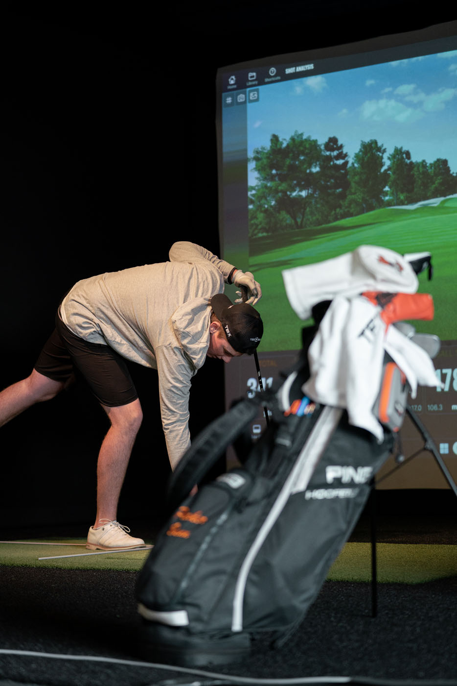 A golfer at Tee Box using our indoor Trackman simulators and their catty bag.
